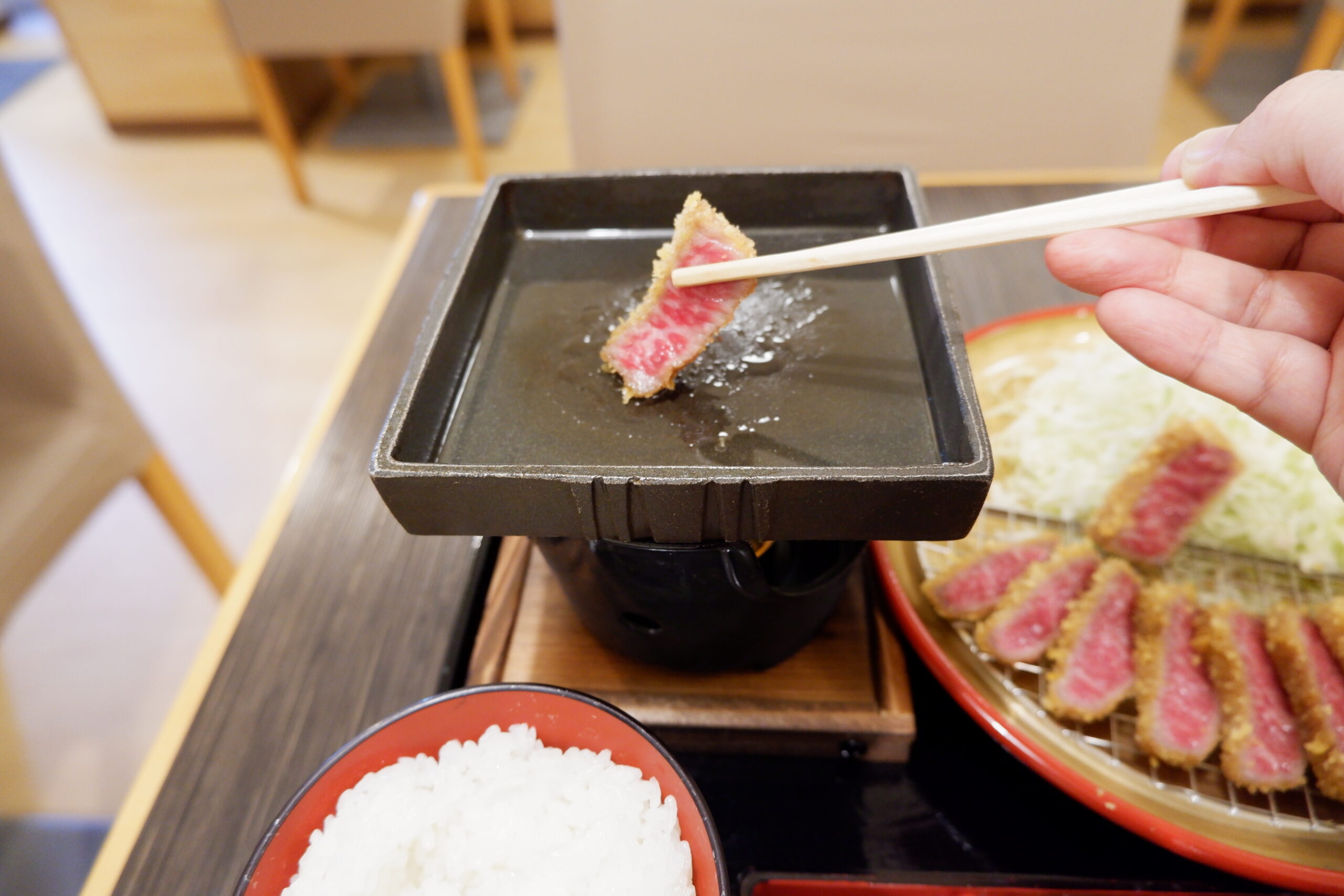 箸でつかんだ牛かつを鉄板で焼いている